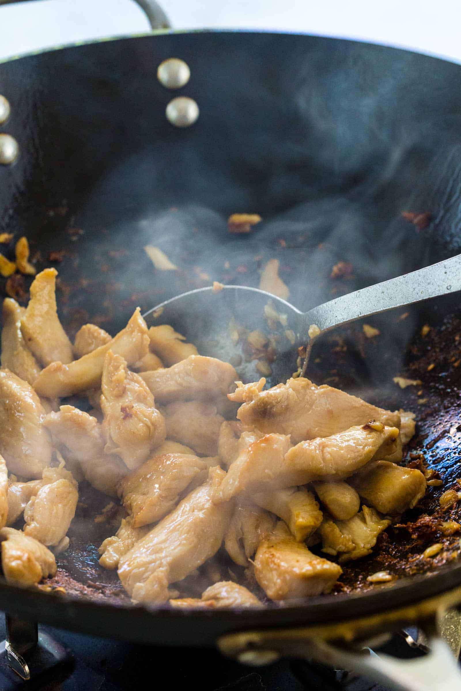 stir frying pieces of chicken in a wok