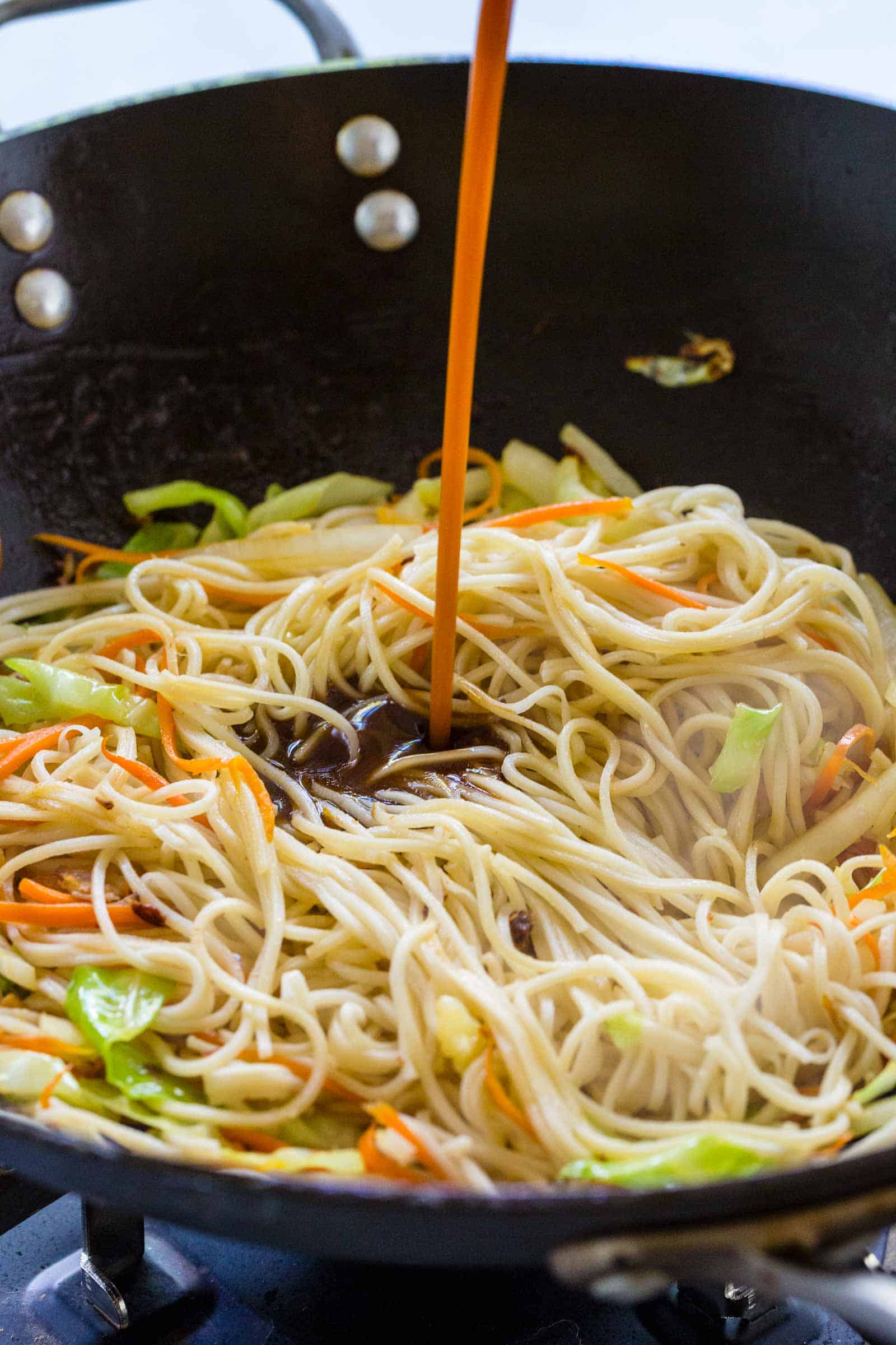 Pouring stir fry sauce onto noodles in a wok