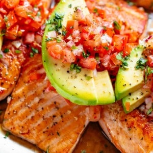 Pan Seared Salmon in a buttery garlic lemon sauce, topped with a fresh tomato salsa and avocado slices!
