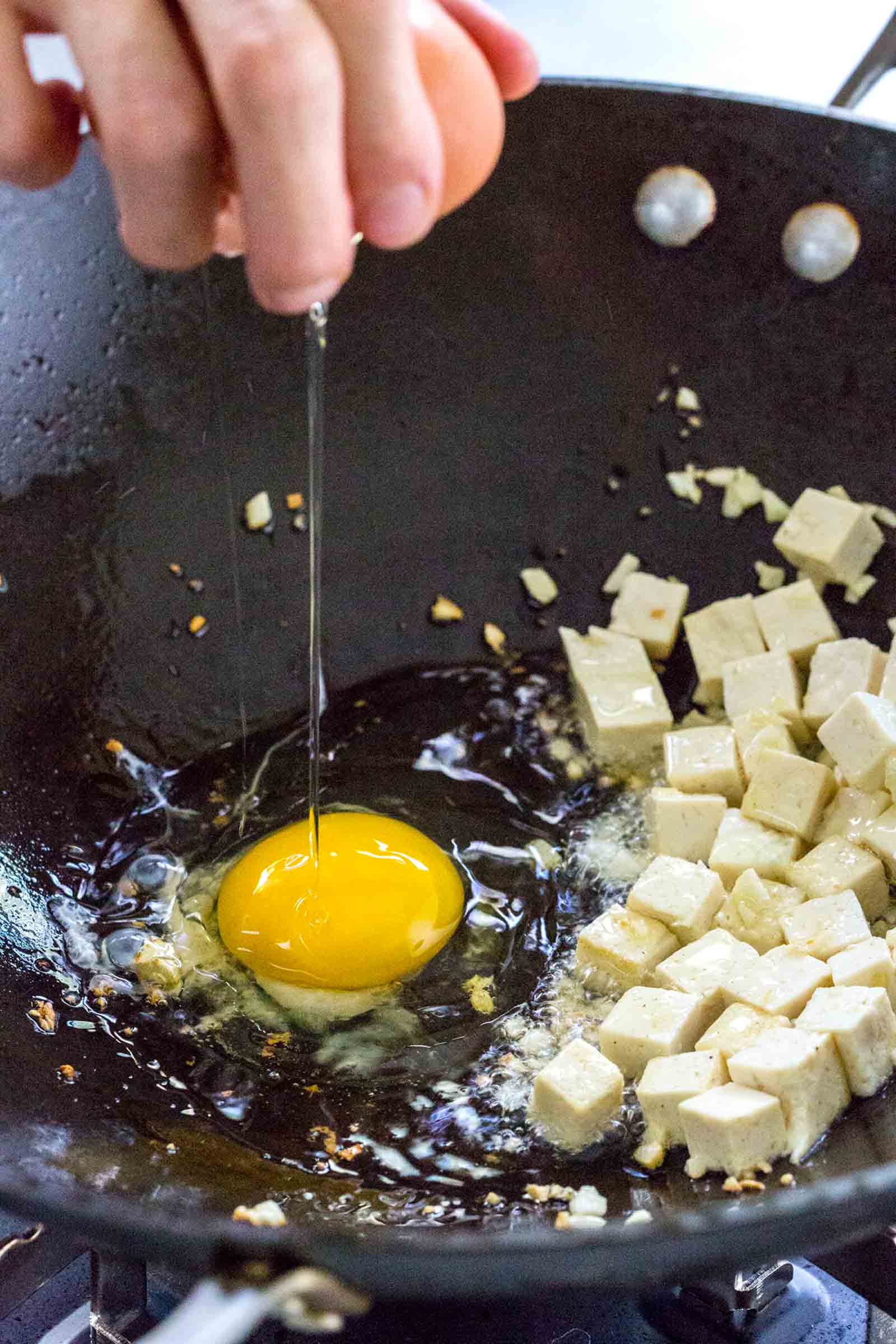 cracking an egg into a wok filled with tofu