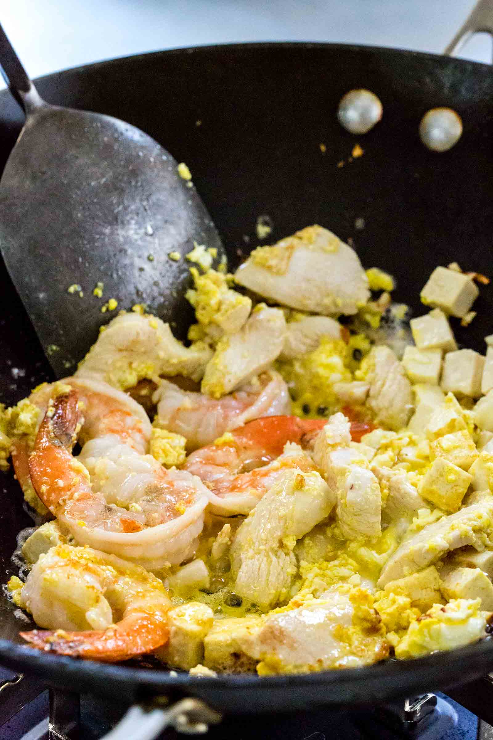 Spatula mixing chicken, shrimp, and eggs into the tofu