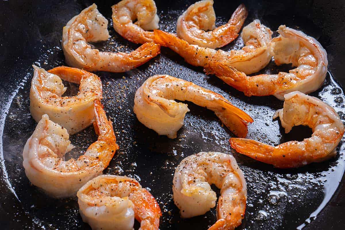 A close-up image of shrimp being heated in a large skillet over medium-high heat.