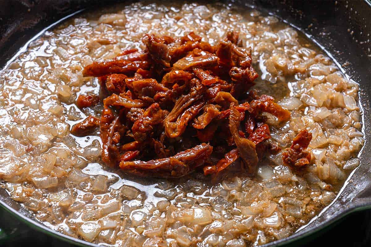 Image of sun-dried tomatoes being added to the onions frying in the butter.