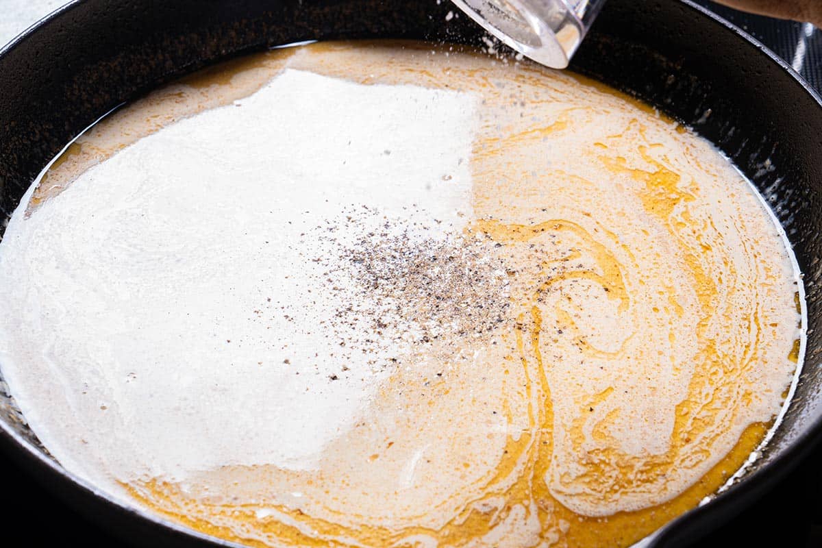 Pepper is being added to the skillet where the cream is being prepared.