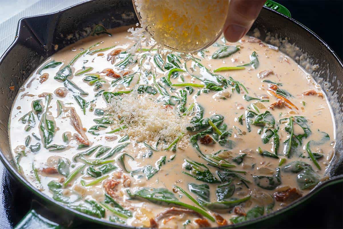 Image of spinach and parmesan being added to the creamy sauce.