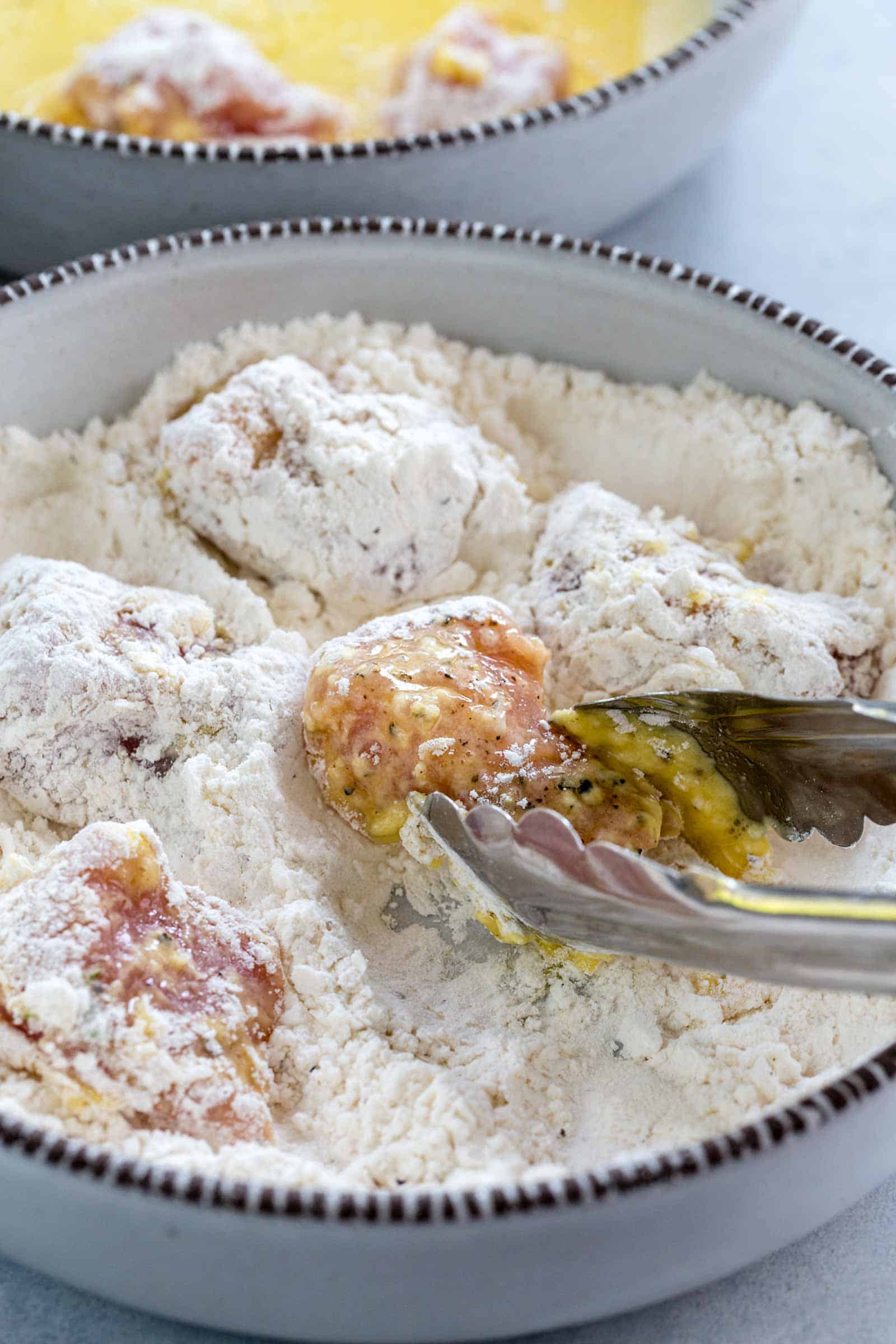 metal tongs dipping pork into flour