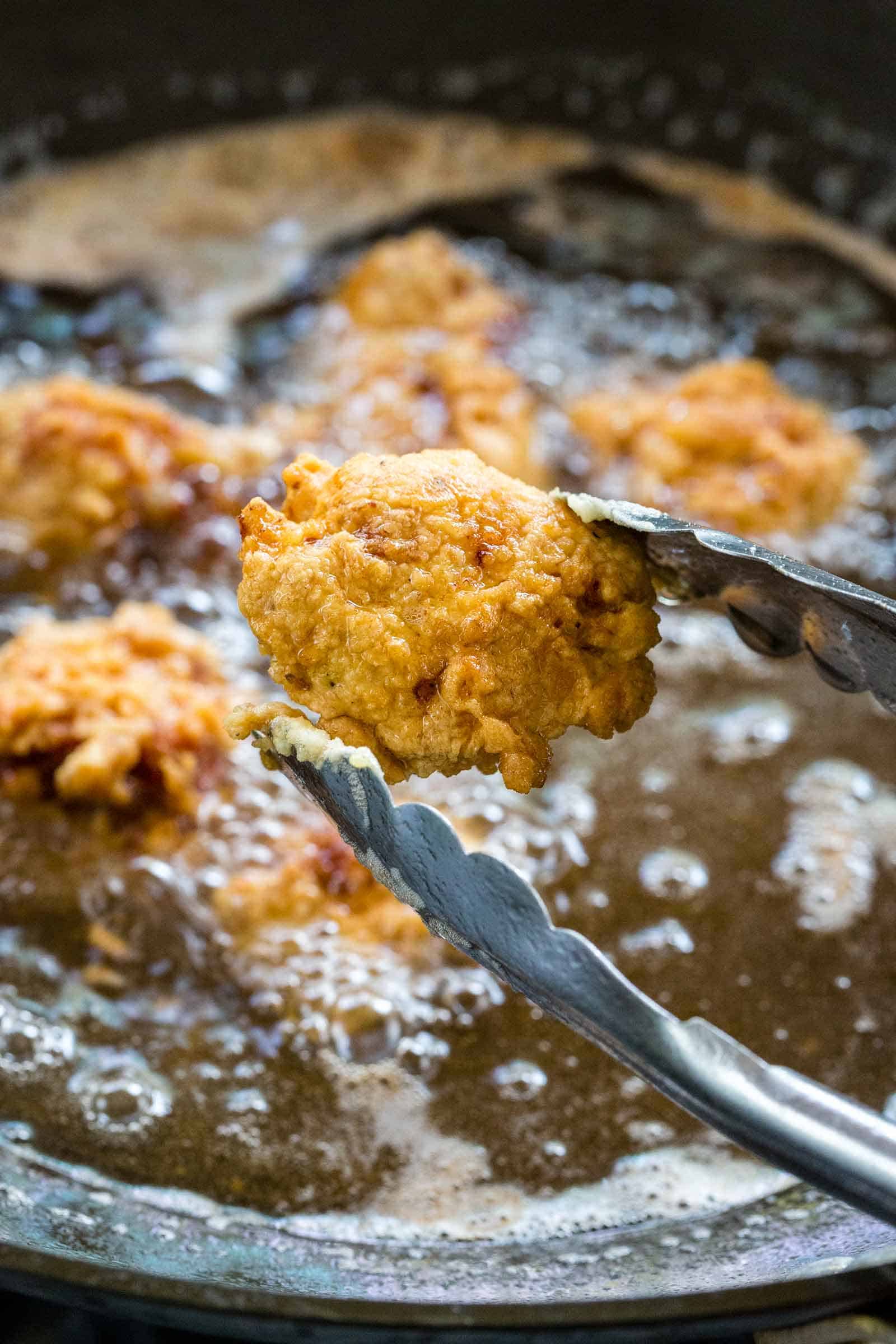 metal tongs holding up a piece of deep fried pork