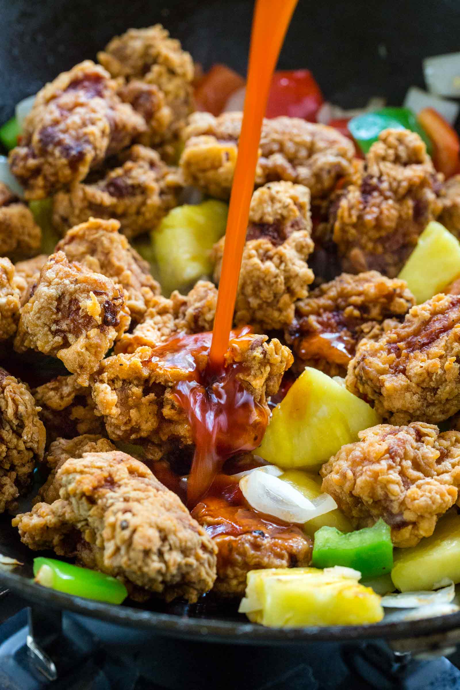 pouring sauce into a wok filled with pork and vegetables