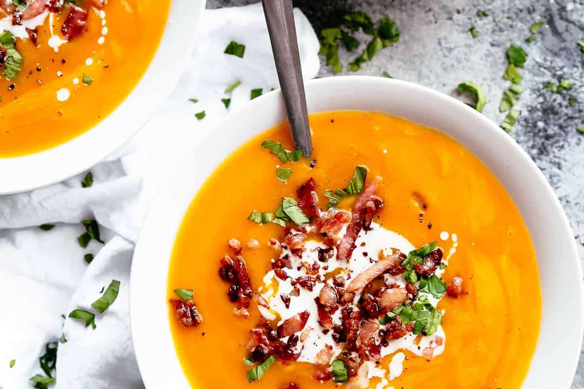 Creamy Pumpkin Soup in a bowl topped with crispy bacon and fresh parsley.