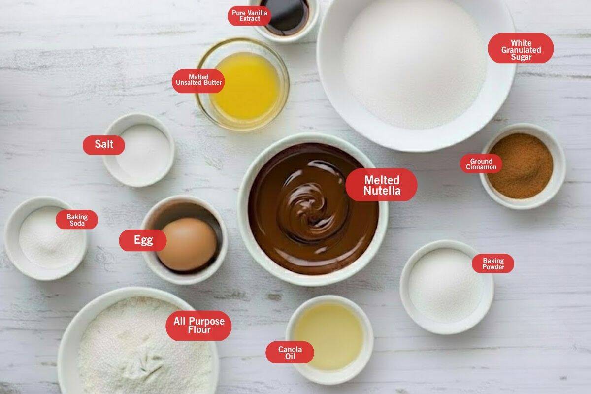 Flat lay of ingredient shot of baking soda and baking powder, all purpose flour, canola oil, baking powder, ground cinnamon, melted nutella, egg, salt, melted unsalted butter, pure vanilla extract, white granulated sugar