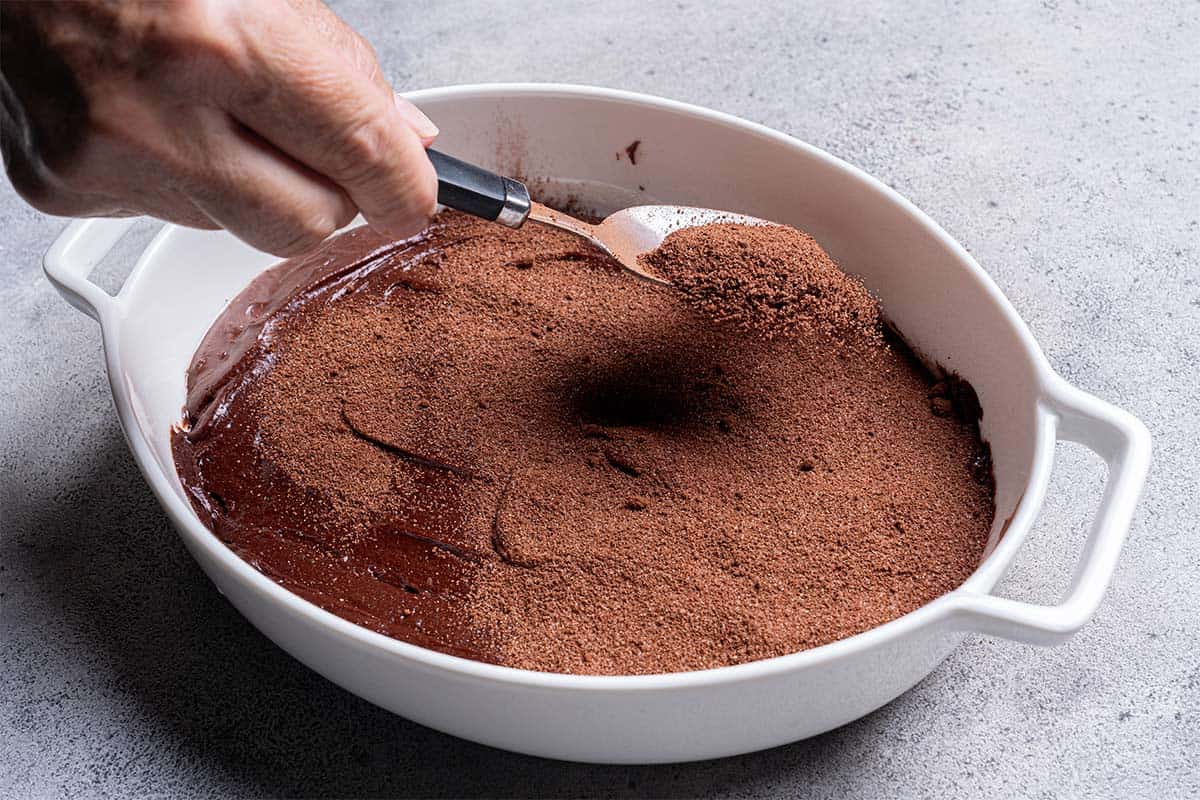 chocolate batter sitting in a pan with dry cocoa mix being sprinkled on top close up