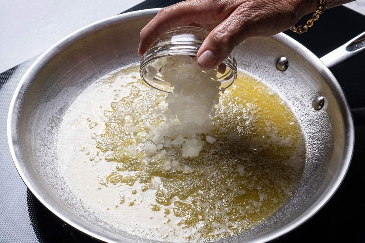 An image of onions being added to the pan containing oil and butter that are frying.