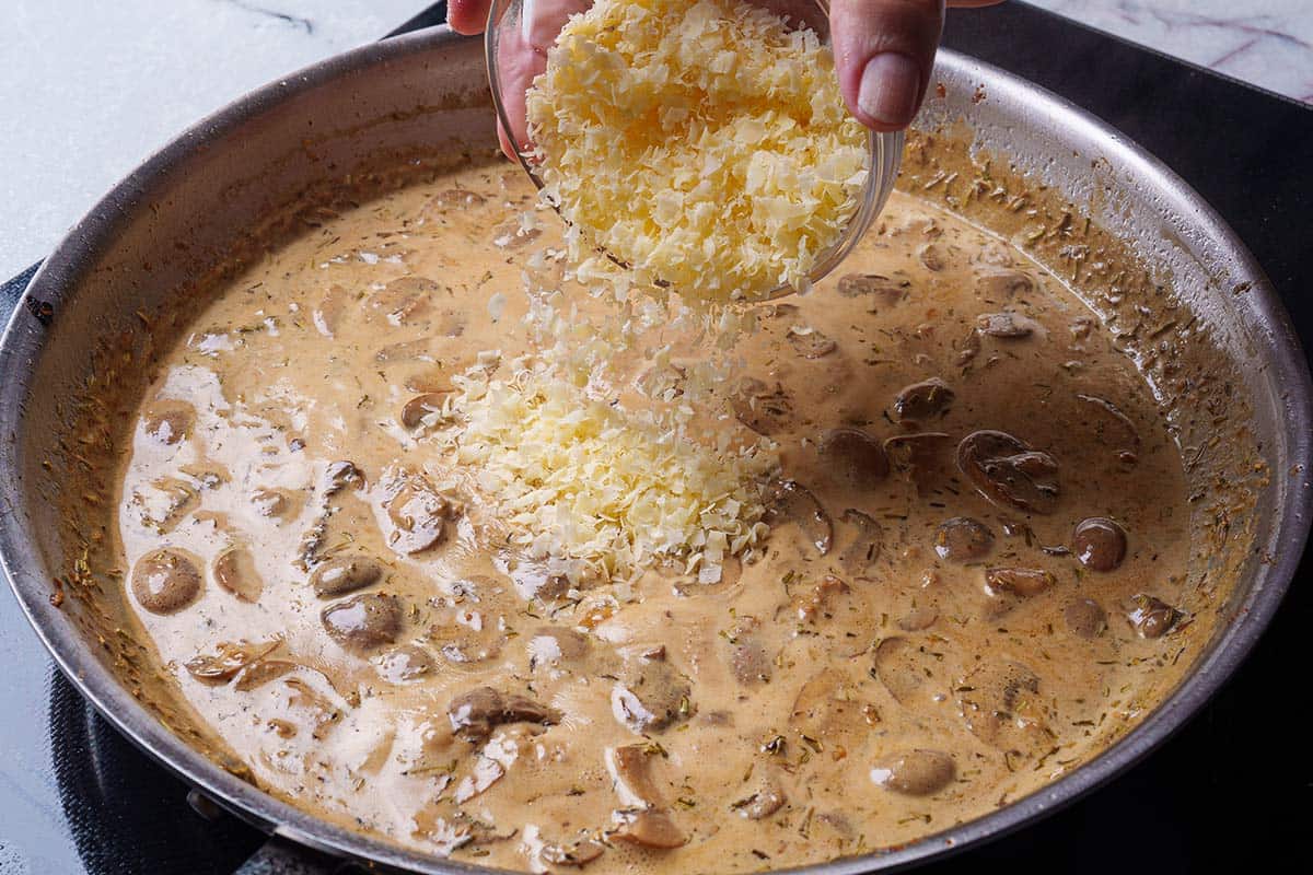 parmesan cheese is poured into a creamy mushroom sauce over a stove in a pan
