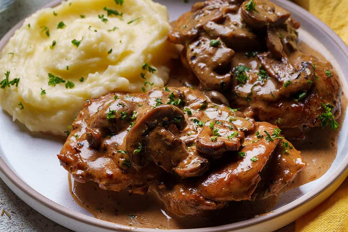 juicy mushroom chicken thighs sit on a plate with mashed potato as a side