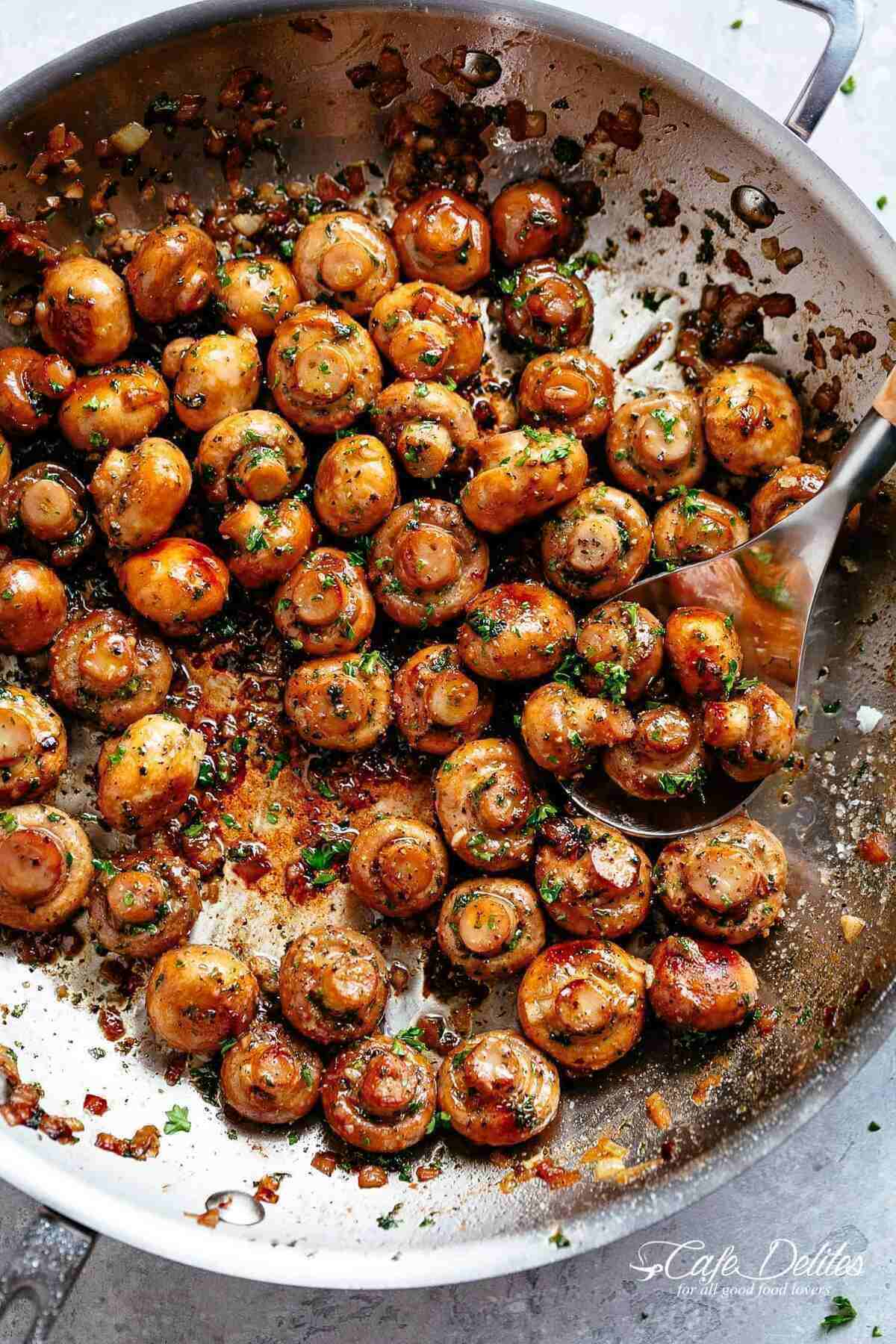 Image of button mushrooms coated in garlic butter sauce, simmering in a pan, ready to be scooped with a kitchen spoon.