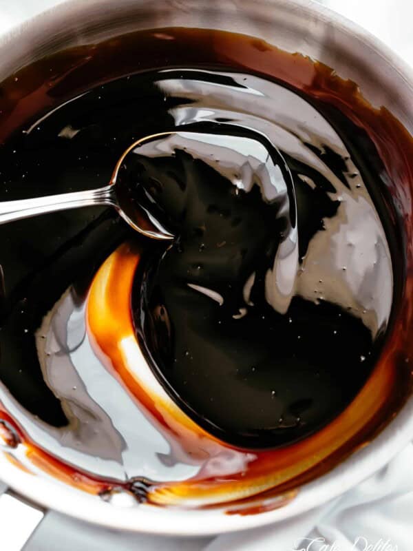 A silver spoon stirring balsamic glaze in a bowl.