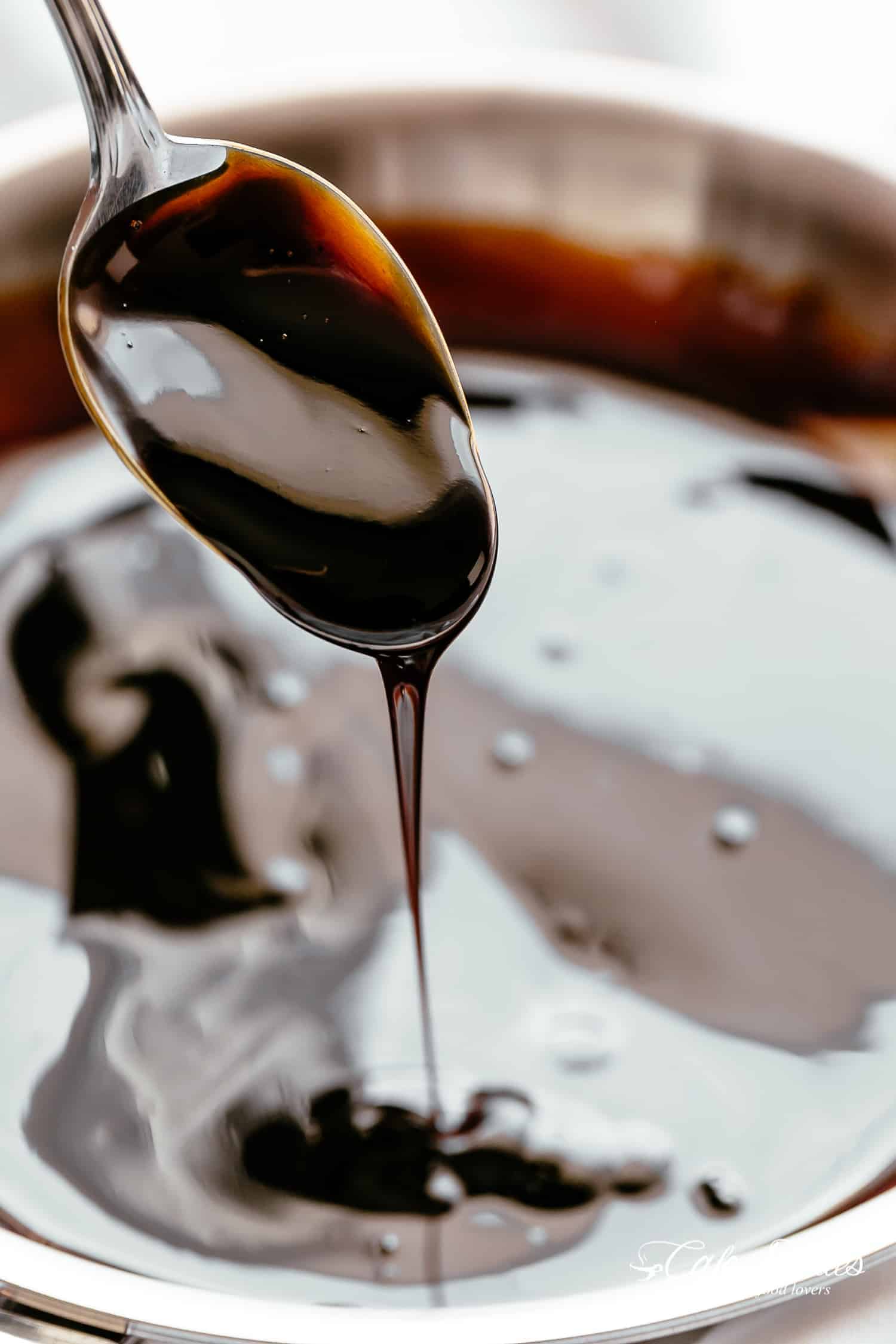 Thick balsamic glaze in a pot with a spoon pouring a scoop of glaze back into the pot. 