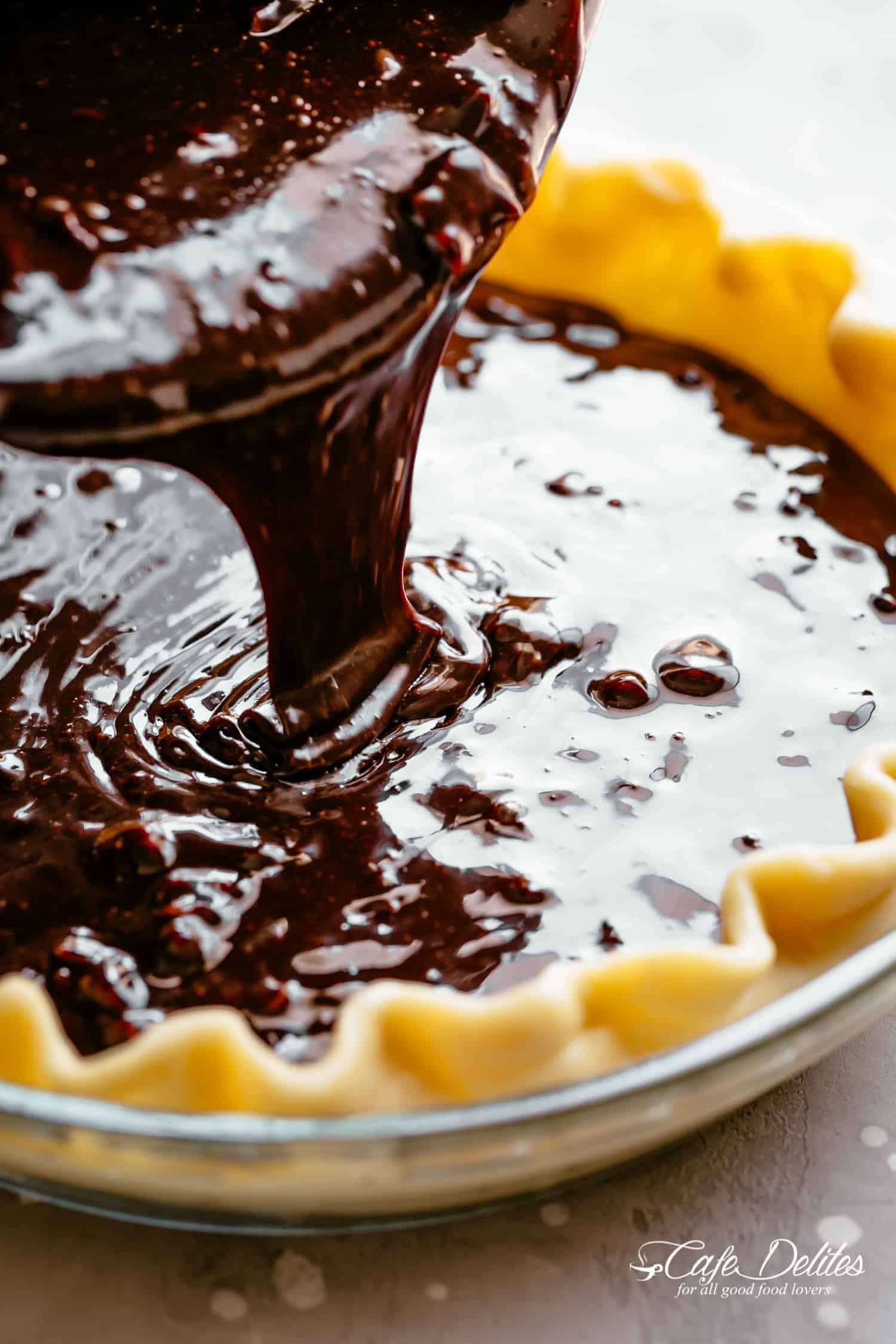 Close up of chocolate sauce being poured into a pie crust before baking. 