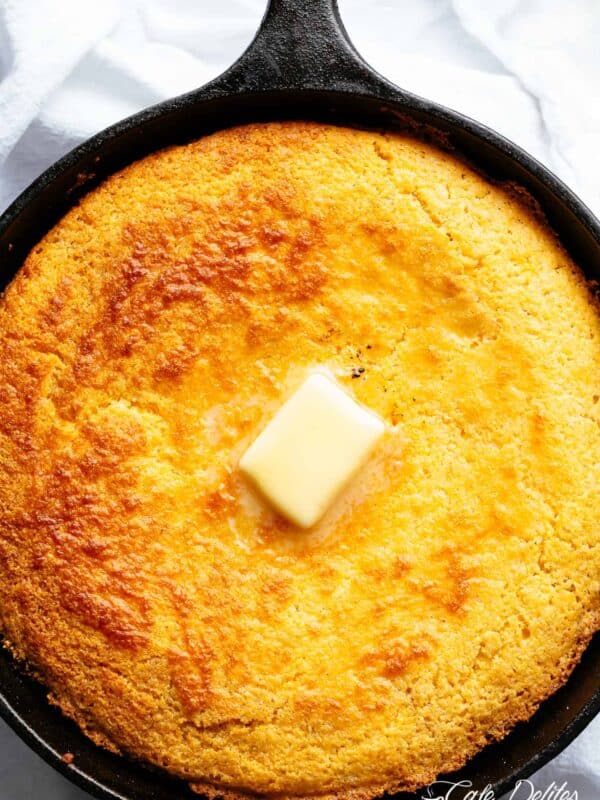 Moist cornbread in a skillet with a golden crust and a melting pat of butter on top.
