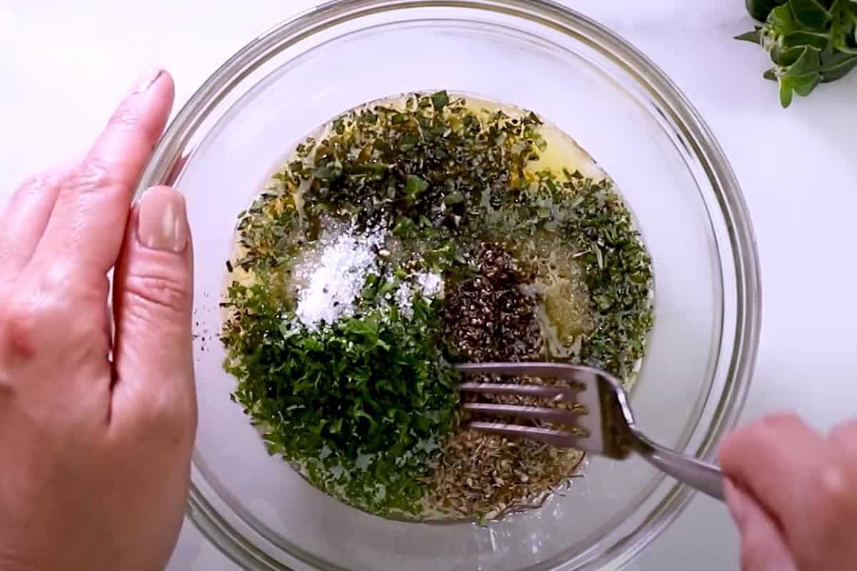 Mixing melted butter, minced garlic, herbs, salt, and pepper in a bowl.
