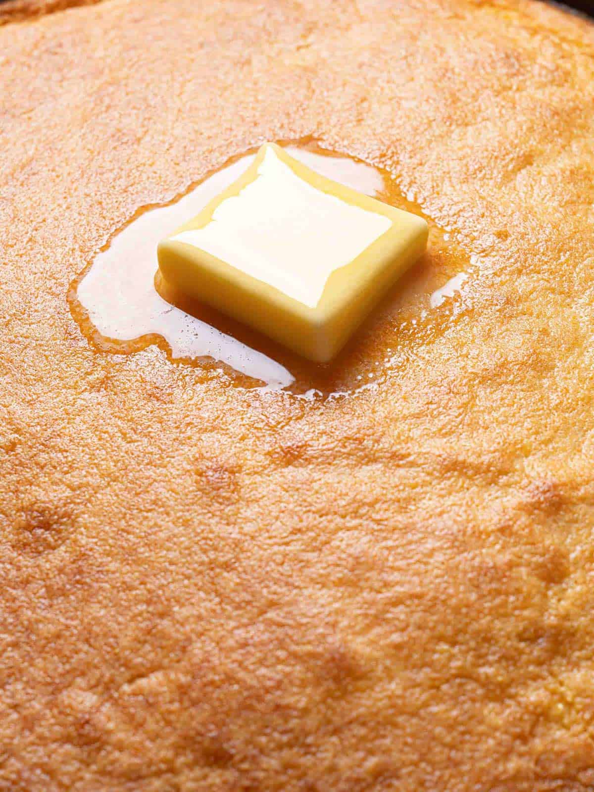 Moist cornbread with a golden crust and a melting pat of butter on top.