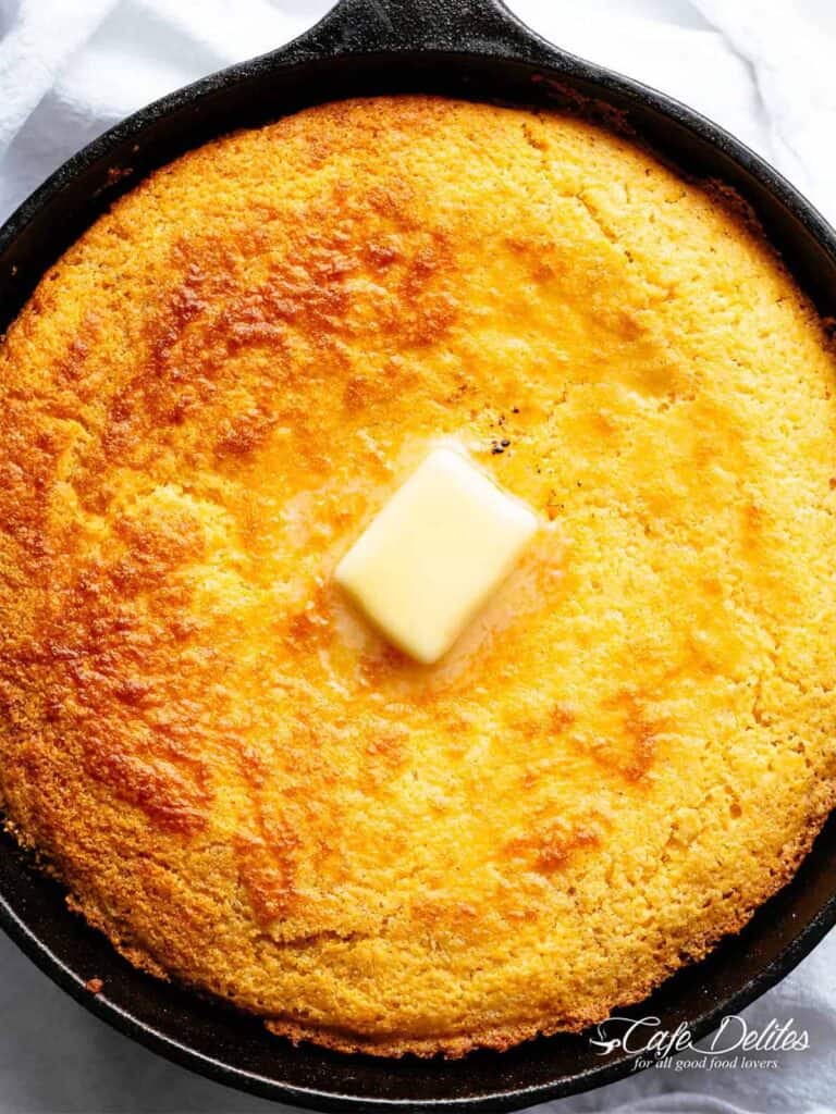 Moist cornbread in a skillet with butter piece in the centre