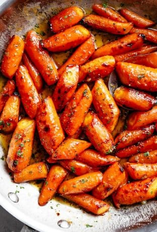 Top view image of Honey Garlic Butter Roasted Carrots in a steel pan with a sprinkle of green garnish.