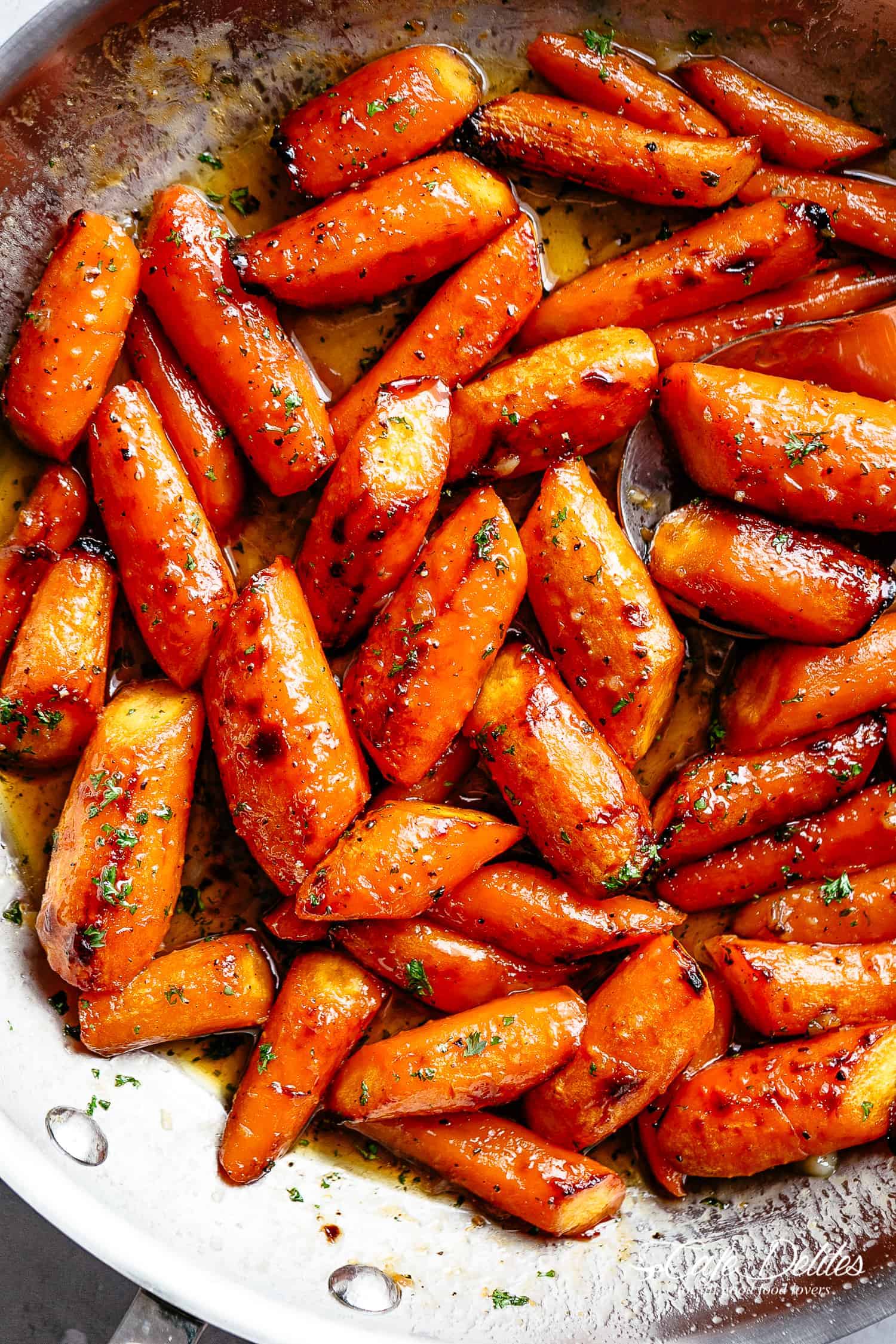 Honey Garlic Butter Roasted Carrots in a steel pan with a sprinkle of green garnish.