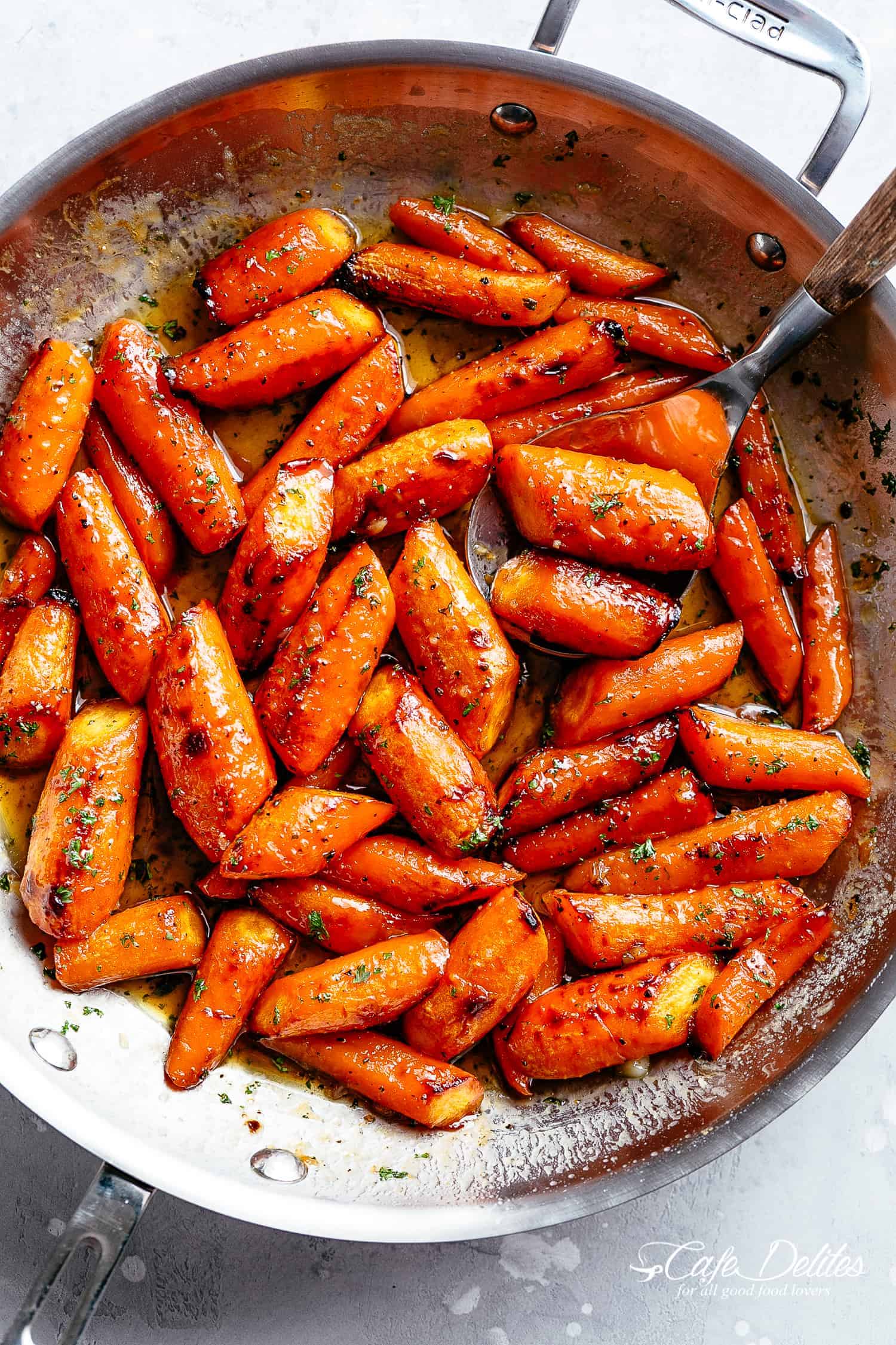 Honey Garlic Butter Roasted Carrots in a steel pan with a sprinkle of green garnish.