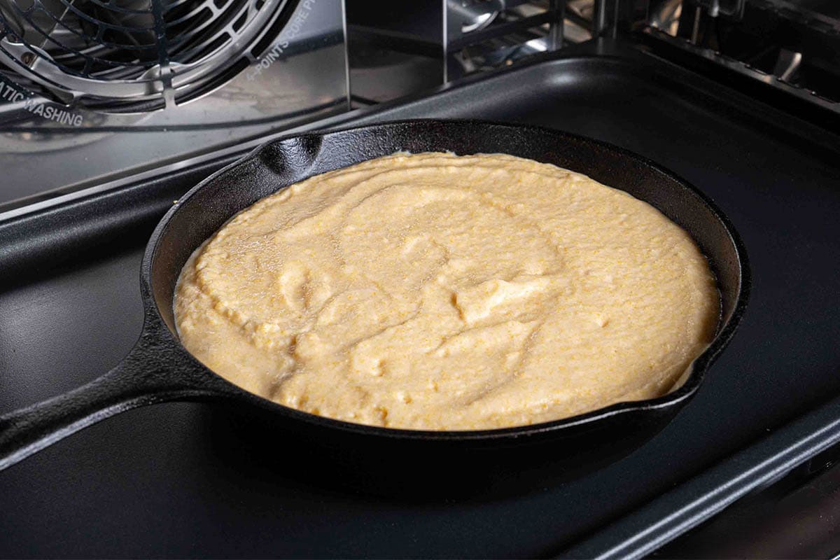 A picture of the skillet with the cornbread mixture being poured into it, ready to be placed in the oven.