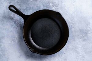 A picture showing a greased skillet on a white marble surface being ready to be put into the oven.