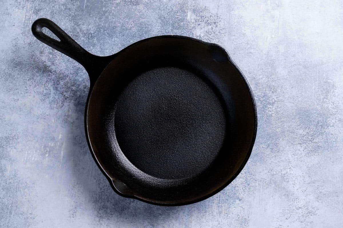 A picture showing a greased skillet on a  white marble surface being ready to be put into the oven.