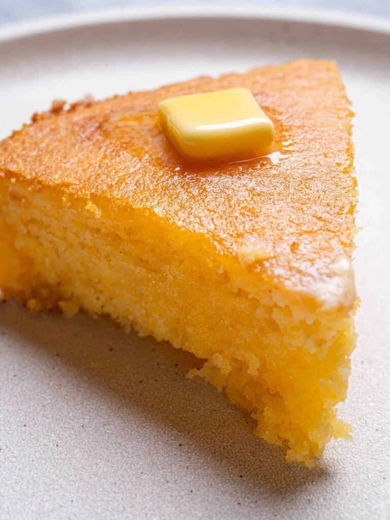 A picture of the moist cornbread recipe, cut and plated, with a knob of butter on top.