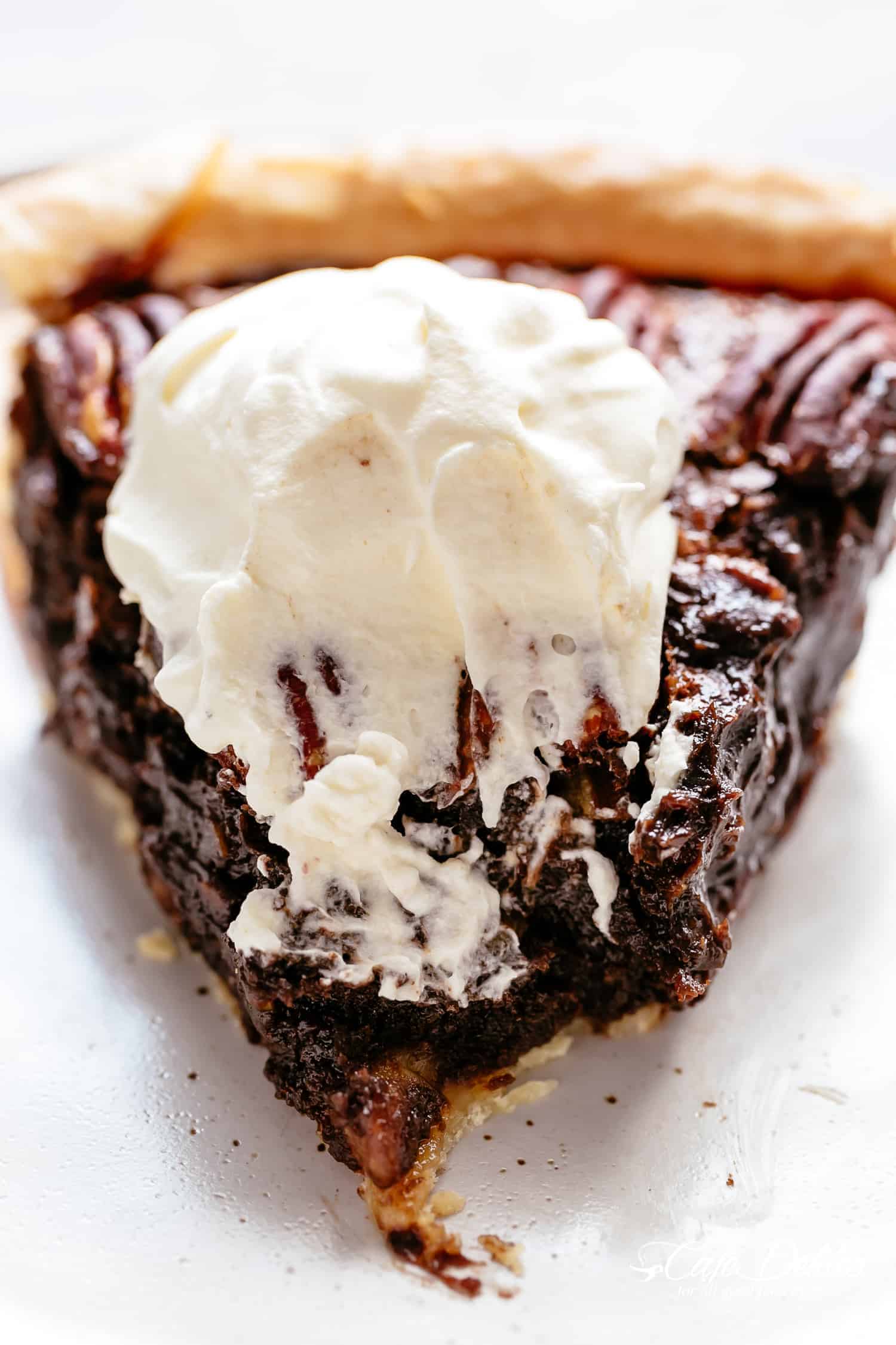 A photo of a chocolate pecan pie with the dollop of cream on top, with the point cut. 