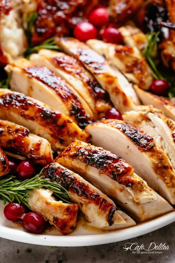 Slices of Roast Turkey on a white plate garnished with cranberries and rosemary sprigs.