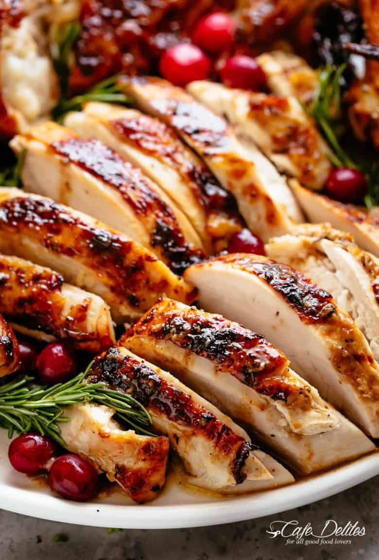 Slices of Roast Turkey on a white plate garnished with cranberries and rosemary sprigs.