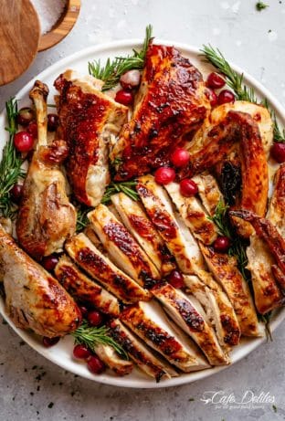 Garlic Herb Butter Roasted Turkey chopped into large slices and pieces, on a serving plate with rosemary sprigs and red cranberries strewn throughout the dish.