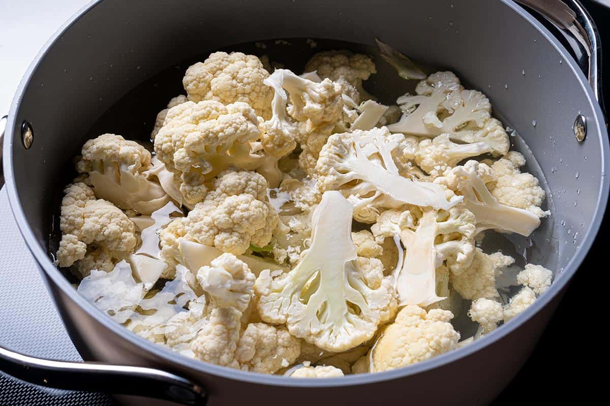 An image of cauliflower being placed in a steamer over a pot of boiling water and steamed until tender.
