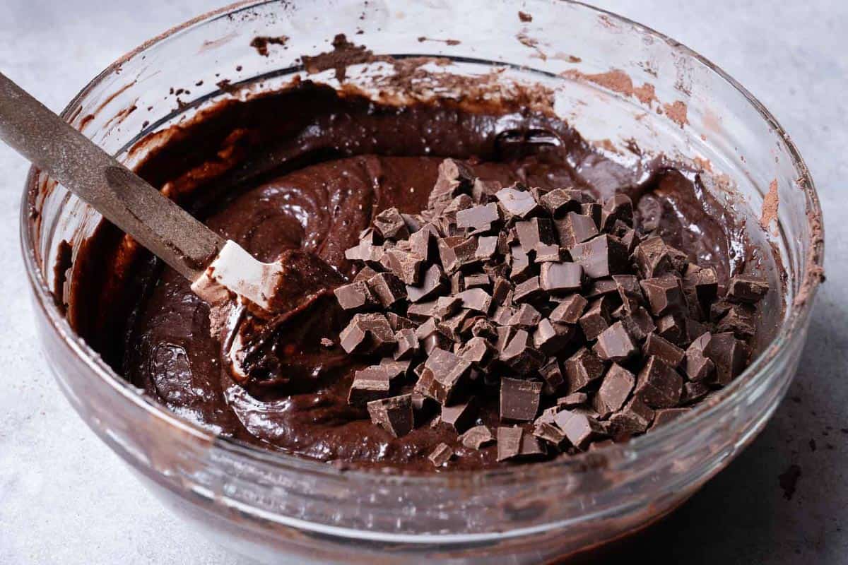 Chocolate chunks are added to the mixture and stirred by a wooden spoon.