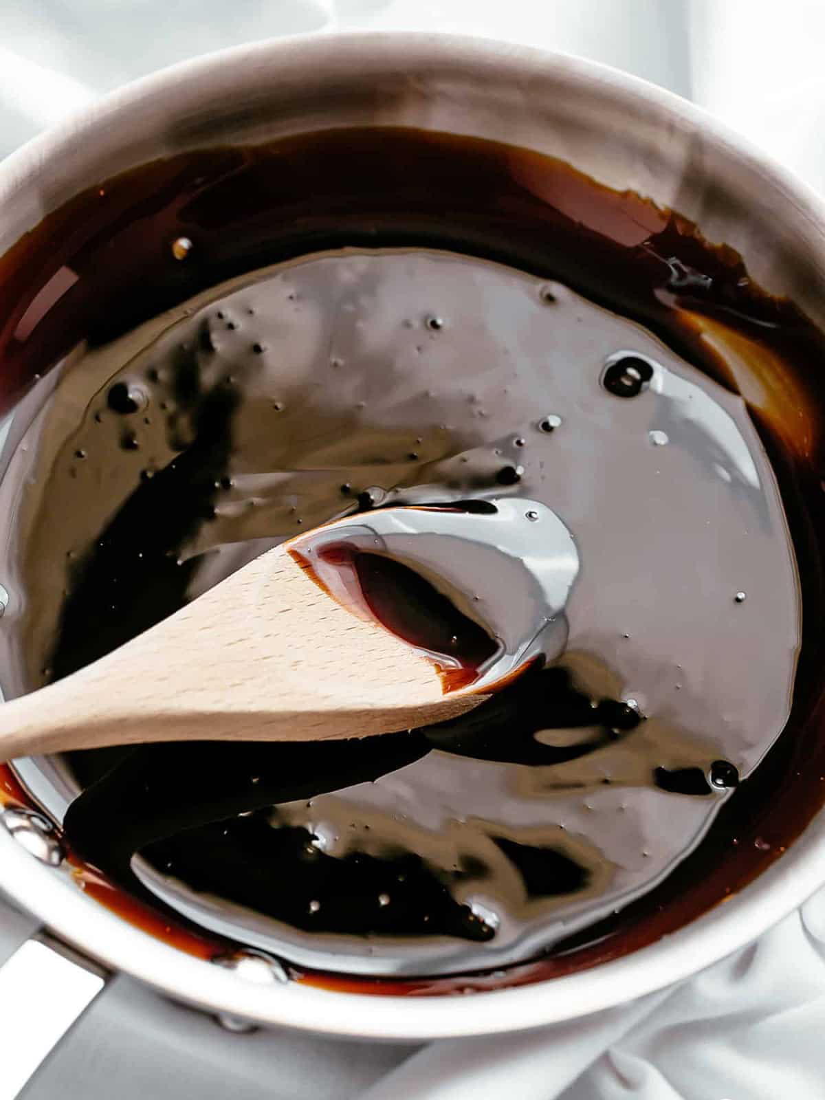 Thick, dark balsamic glaze being mixed with a wooden spoon in a bowl.
