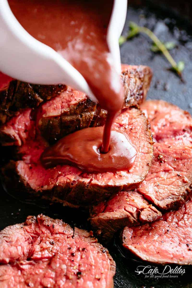 Close up of a red wine sauce drizzling from a white cup over slices of the juicy Beef Tenderloin Roast. 