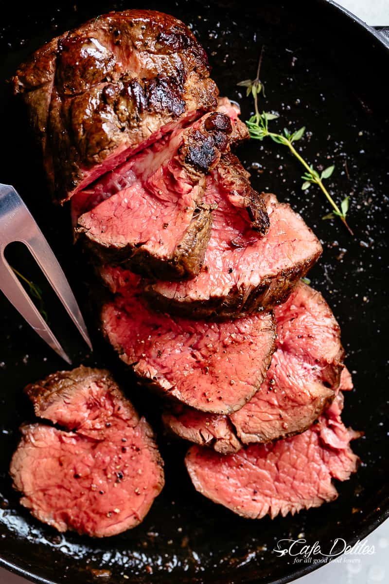 Juicy roast Beef Tenderloin sliced to show the juicy pink meat, in a black skillet.