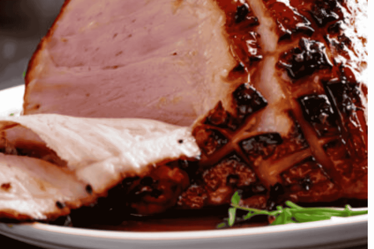 close up shot of the ham, side profile showing the slices on a plate with some green leaves on the bottom of the plate and glaze dripping