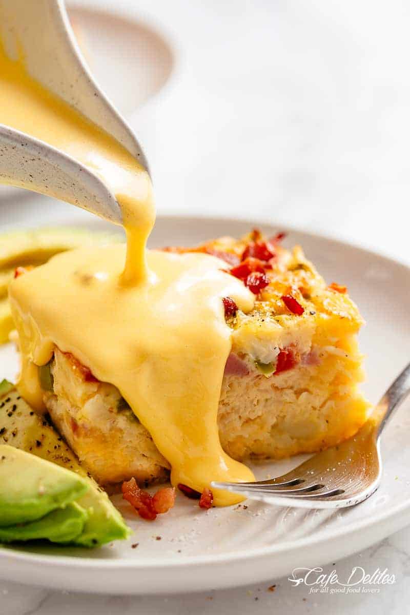 Hollandaise sauce being poured over a slice of breakfast casserole on a plate. 