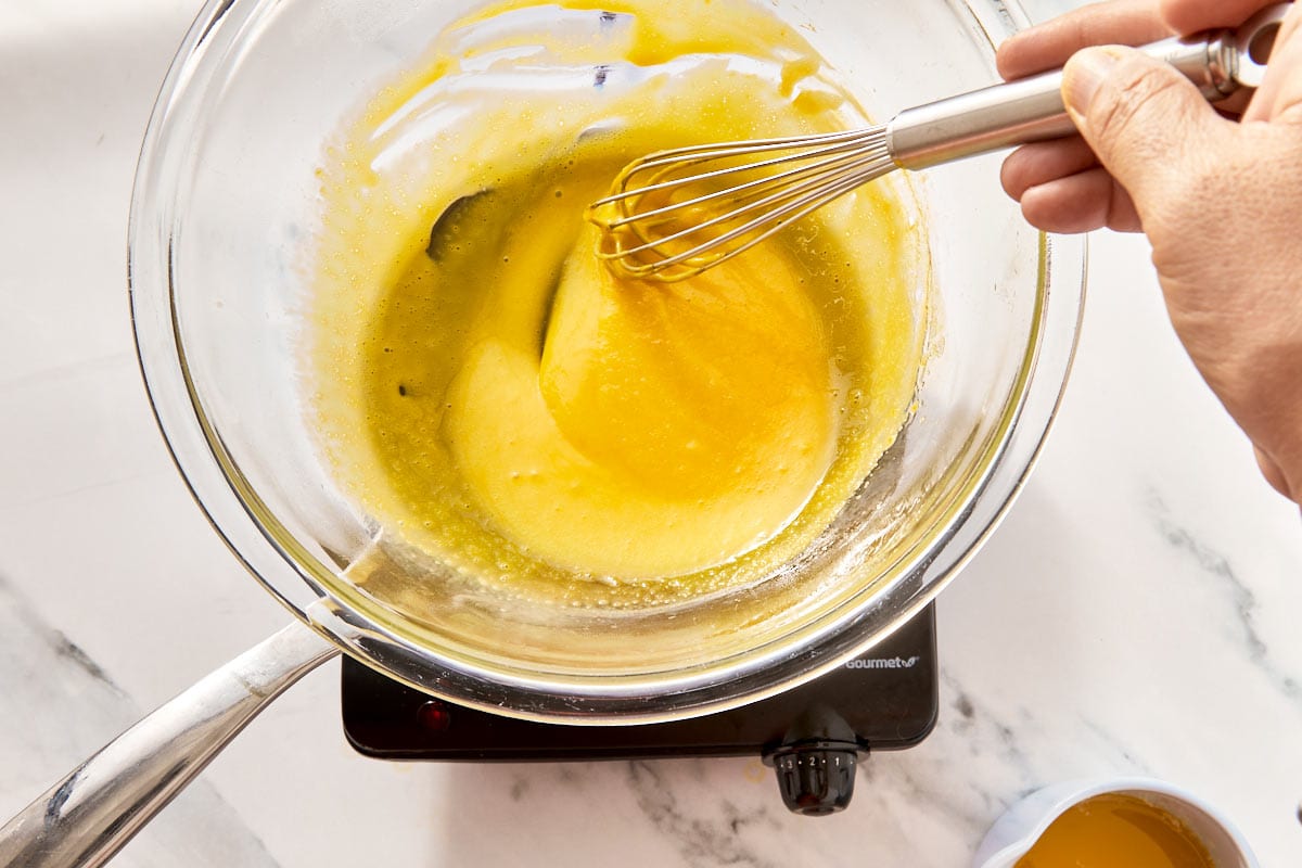 Hot melted butter being slowly poured into the yolk and lemon mixture.