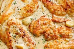 Three chicken breasts with a crispy golden outer coating in a mouth-watering garlic cream sauce with whole garlic cloves.