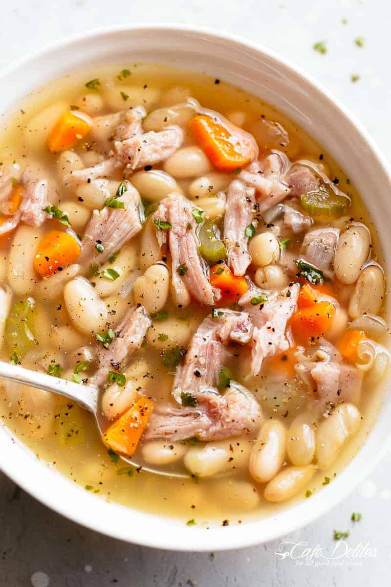 Close-up image of a hearty ham and bean soup in a white bowl, with a spoonful being lifted, showcasing the tender beans and chunks of ham.