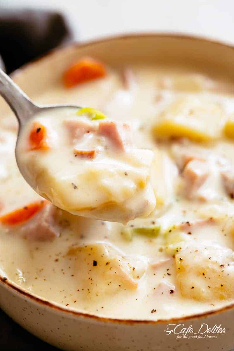 A soup spoon scooping ham and potato soup from a single serve bowl. 