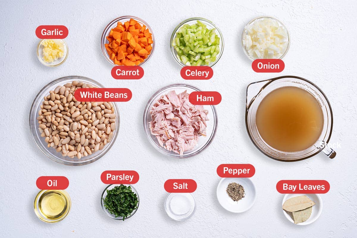 Image with all the ingredients needed for the preparation of this recipe, specifically: garlic, carrot, celery, onion, white beans, ham, chicken broth, oil, parsley, salt, pepper, bay leaves.