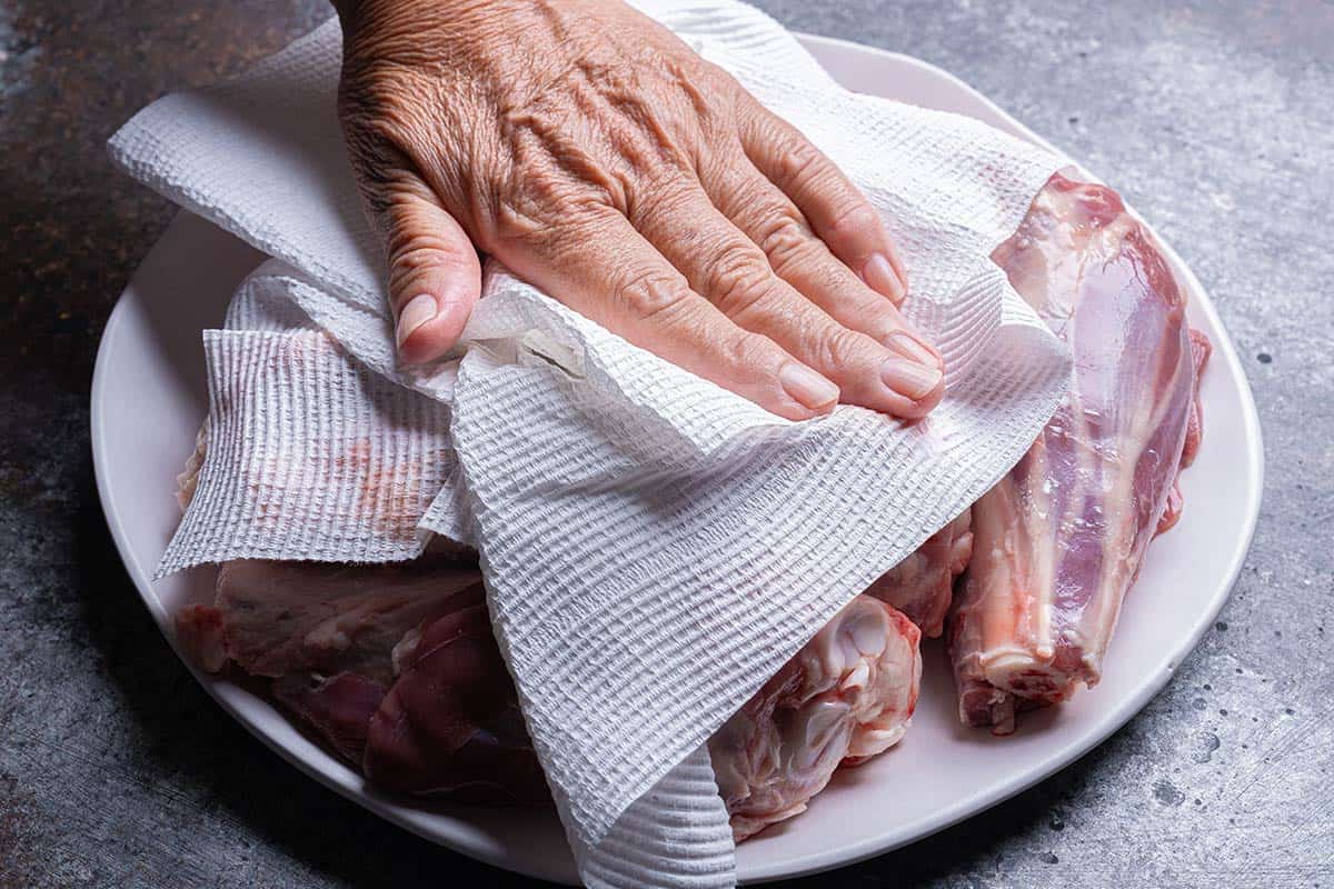 Patting dry lamb shanks on a plate